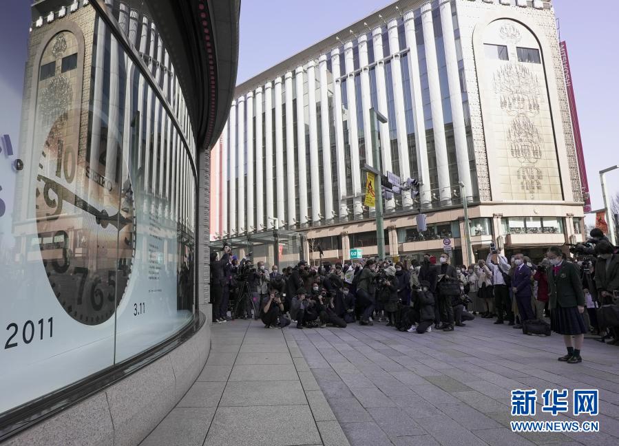 3月11日、東京・銀座で、「東日本大震災から10年」と映し出された大型モニターの前で犠牲者に哀悼の意を捧げる人々。