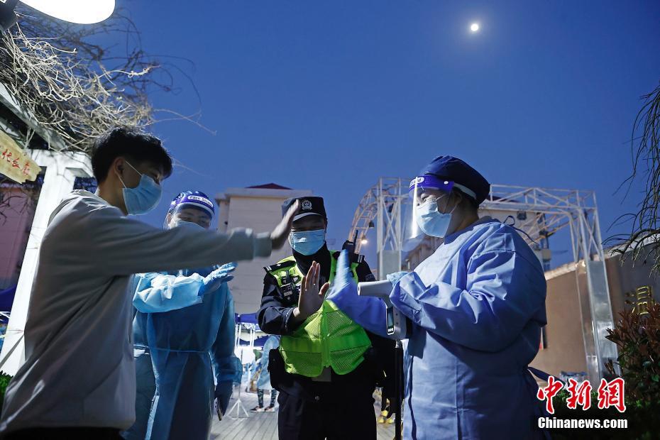 虹橋空港新村で15日、警察官に率いられ、PCR検体採取前の検温を受ける住民（撮影・殷立勤）。