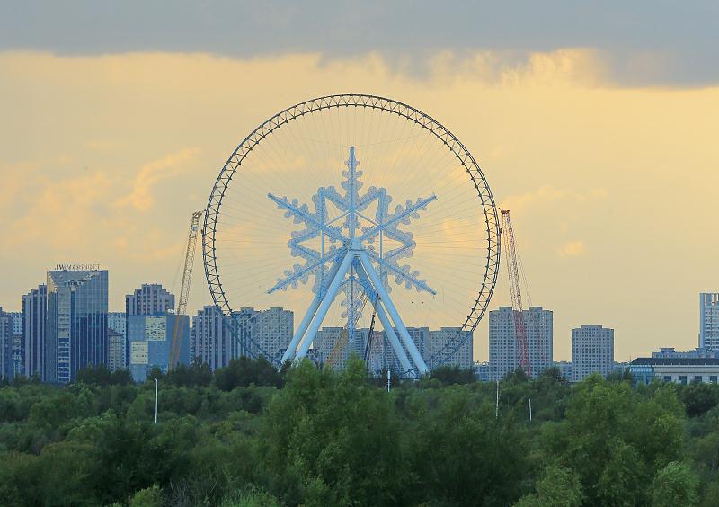 8月24日、黒竜江省哈爾浜（ハルビン）氷雪大世界で、建設中の観覧車の「雪の結晶」取り付け工事がこのほど完了、松花江のほとりに巨大な雪の結晶が出現。（写真著作権はCFP視覚中国が所有のため転載禁止）