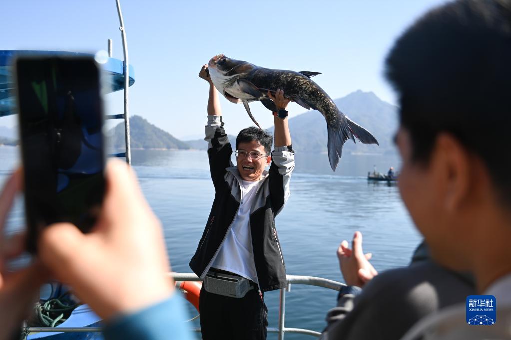 浙江省杭州市淳安県千島湖の黄山尖水域で、捕獲したばかりの「魚の王様」を両手で掲げる観光客（10月22日撮影・黄宗治）。