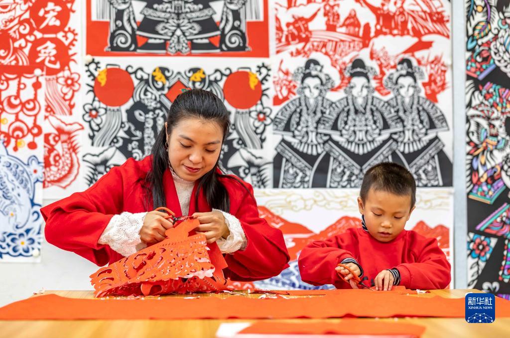 黔西市文化館のアトリエで、新年を迎える伝統工芸の「切り紙」作りを学生に教える、黔西切り紙無形文化遺産伝承人の岳紅霞さん（写真左、12月26日撮影・範暉）。