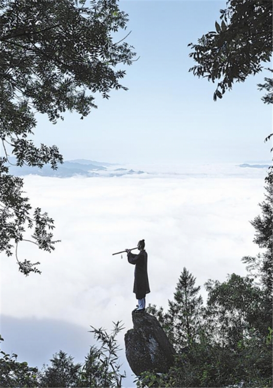 8月19日、白馬山天馬峰の頂上の石の上に立ち、眼前に雲海が広がる中、中国の伝統楽器「洞簫」の練習をするポーランド人のダリウスさん。